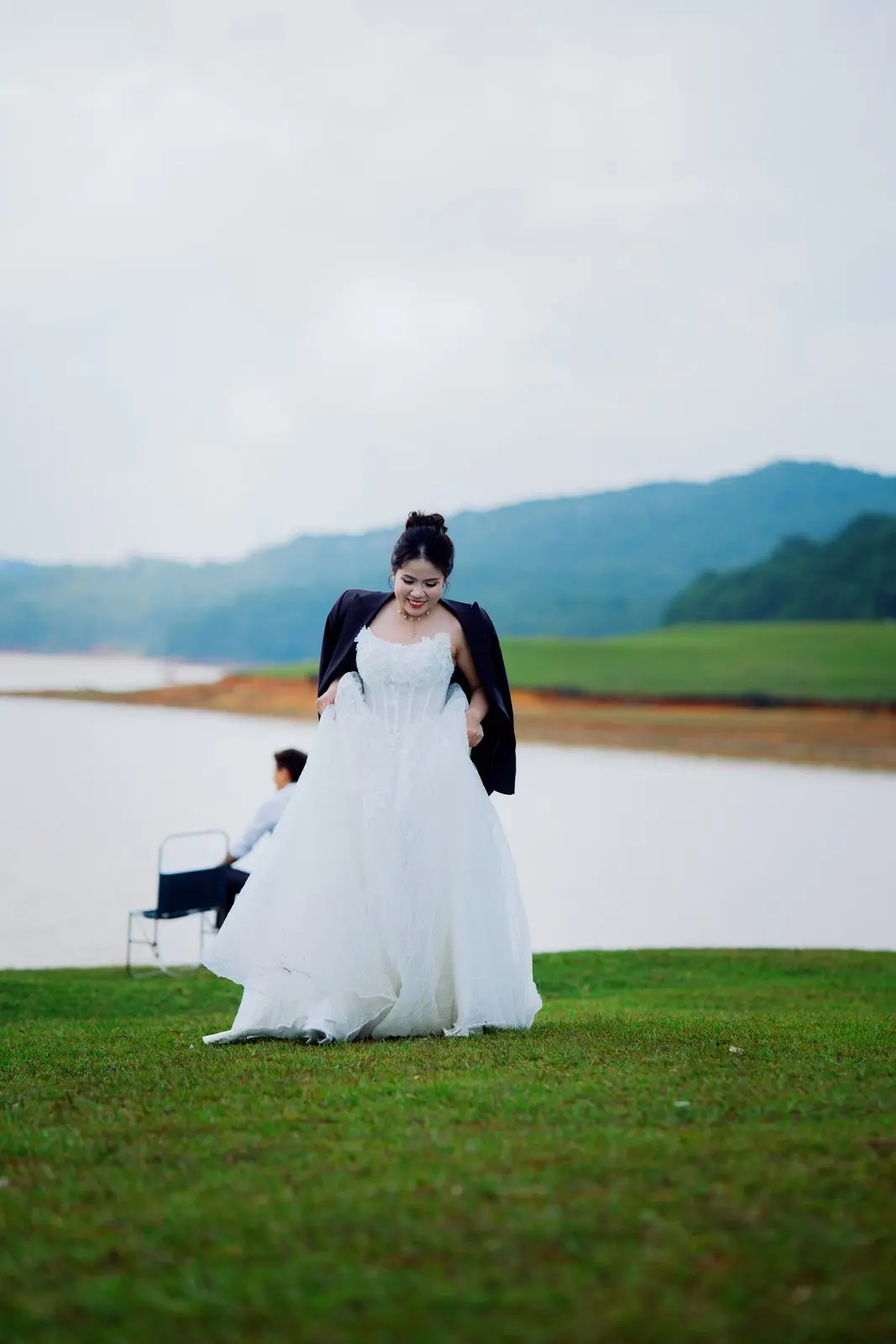 Loo mặc váy cưới đứng trên bãi cỏ bên hồ