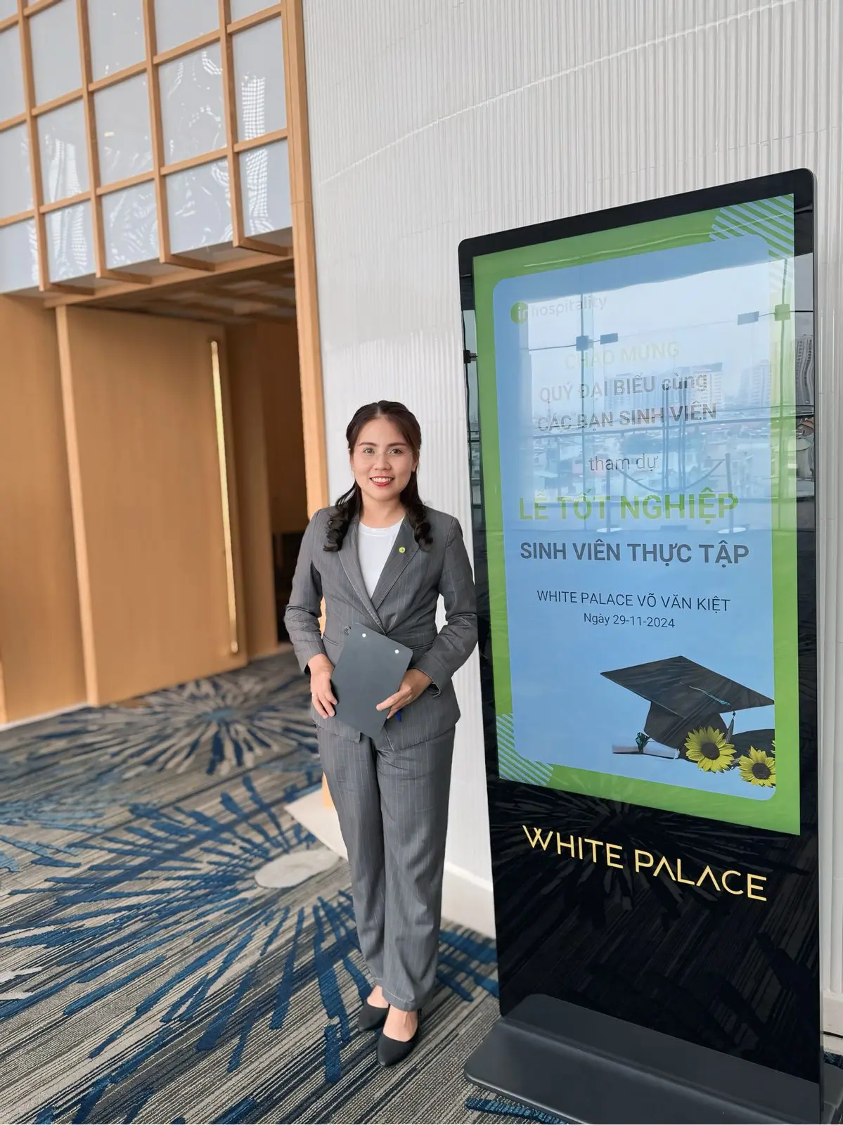 Loo mặc vest xám đứng cạnh bảng lễ tốt nghiệp sinh viên thực tập ở White Palace