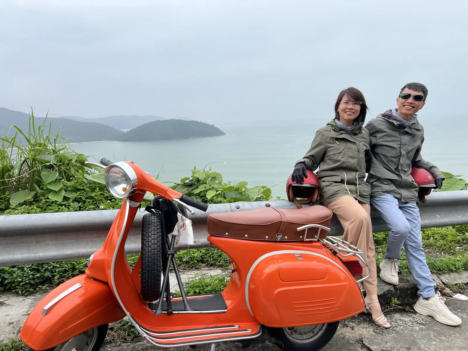 Loo và Boo ngồi bên chiếc Vespa cam trên đèo Hải Vân, biển phía sau