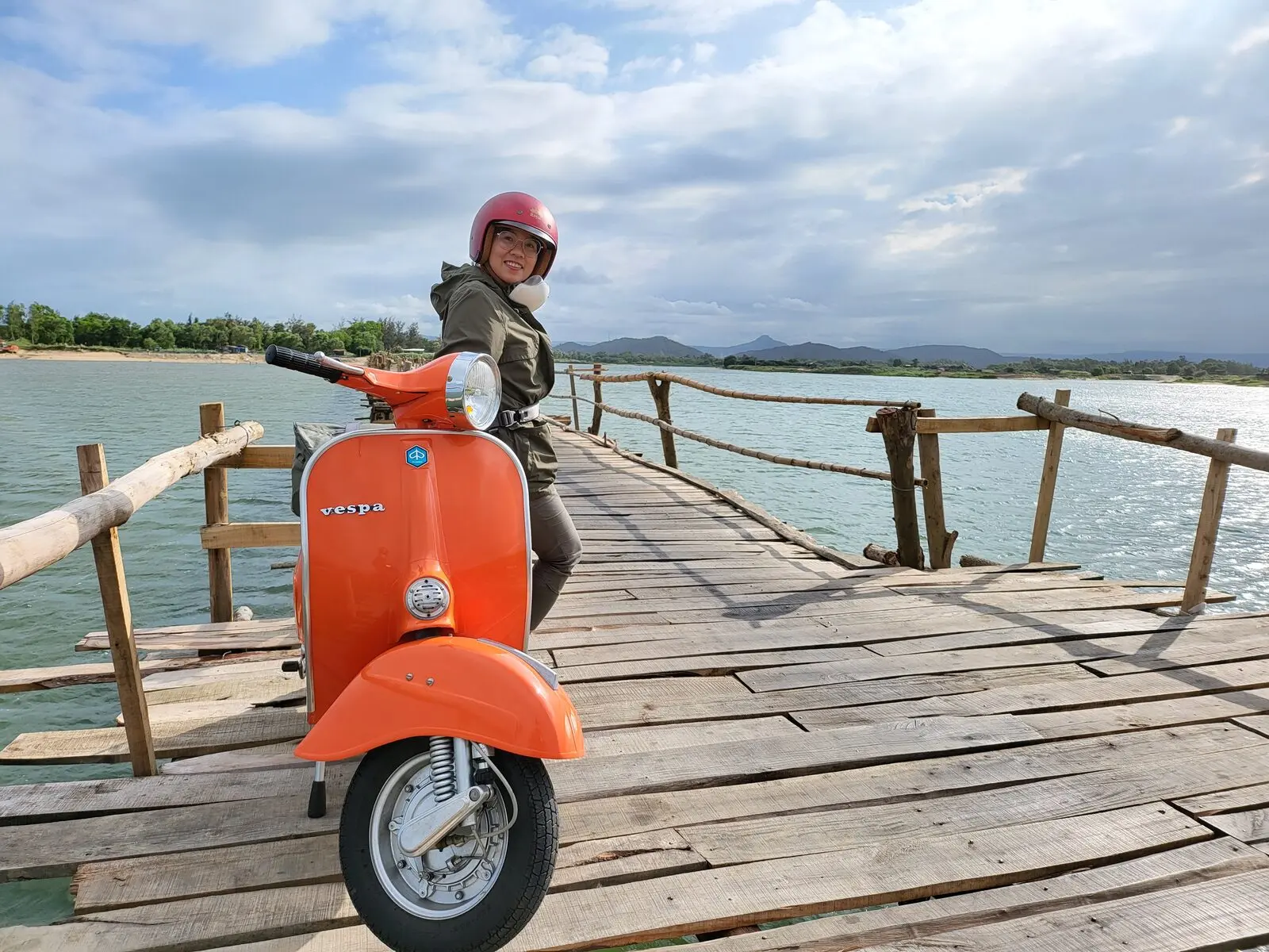 Loo đội mũ bảo hiểm bên chiếc Vespa cam trên cầu gỗ ra biển