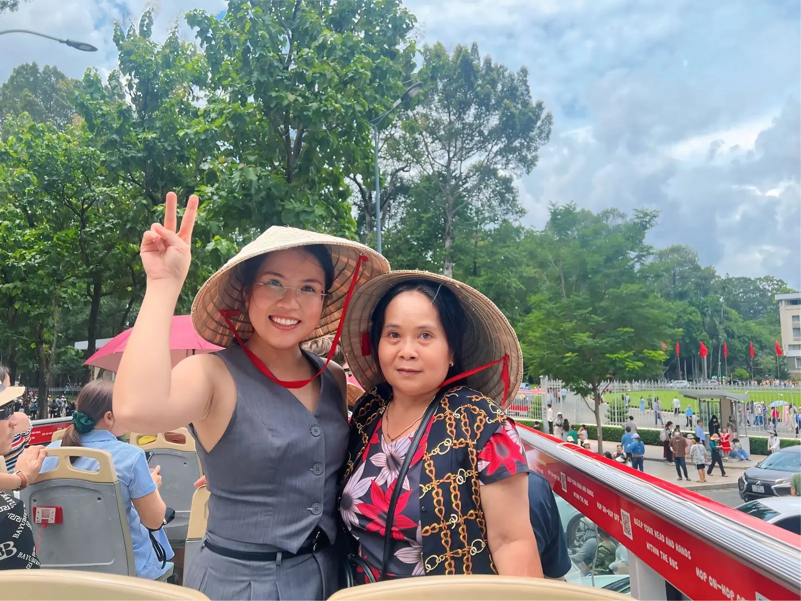 Loo đội nón lá giơ tay chữ V cùng một người thân trên xe buýt hai tầng
