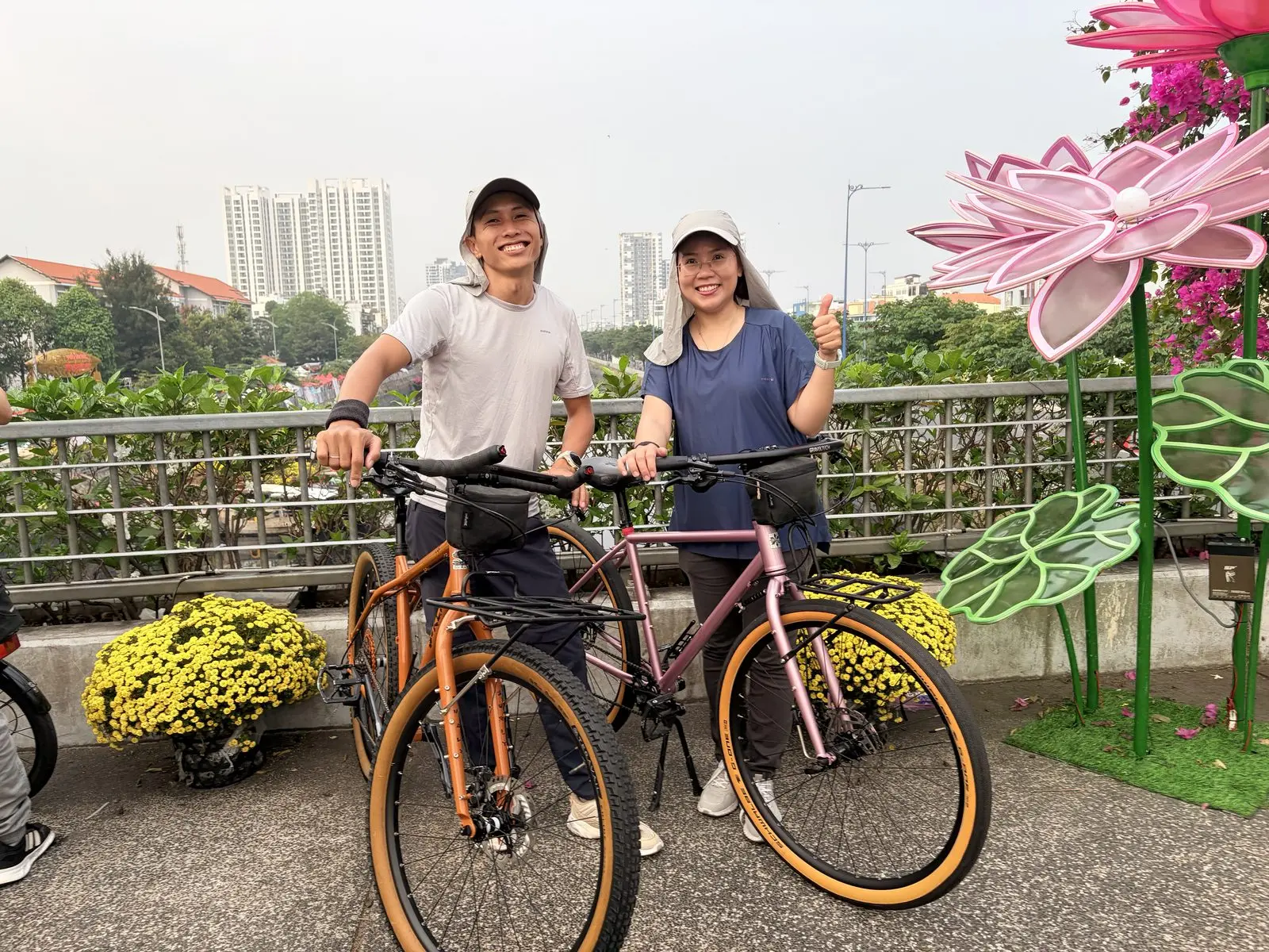 Loo và Boo đứng cạnh hai chiếc xe đạp bên những chậu hoa Tết