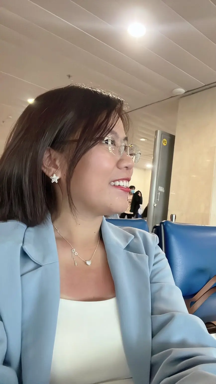 Loo mặc vest xanh nhạt, ngồi chờ ở sân bay
